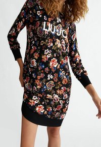 Květinové šaty mikinového střihu v černé barvě s barevnými květinami. Disponují elastickými manžetami a spodním lemem, s bílým logem "LIU JO" na prsou.
