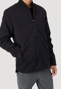 Giubbotto bomber nero con zip frontale, collo a coste e tasche laterali. Realizzato in un tessuto liscio e resistente con dettagli di cucitura minimi.