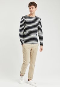 Langærmet skjorte i marineblå og creme striber, parret med beige chinos og hvide sneakers. Skjorten har en rund halsudskæring og en tætsiddende pasform.