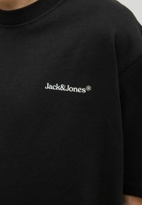 Tricou din bumbac negru cu mâneci scurte, cu un logo alb "Jack&Jones" pe piept. Gât rotund cu nervuri, textură fină.