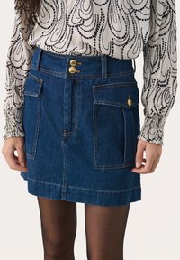 Tummansinisestä denimsatiasta valmistettu hame, jossa on kaksi etutaskua, sivupaikallinen kiinnitys ja näkyvät tikkausompeleet. Kevyt kangas, jolla on sileä rakenne.