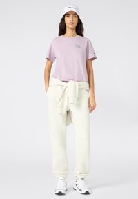 Light purple t-shirt with a small logo, paired with cream sweatpants and a white cap, creating a casual layered look.