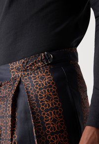 Falda de seda con una base azul oscura y un patrón floral naranja, acentuada por una hebilla metálica en la cintura y detalles de pliegues planos.
