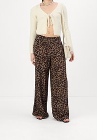Pull beige court avec détail à nouer à l'avant, associé à un pantalon large à imprimé léopard dans les tons marron et noir. Sandales à talons noires.