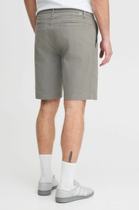 Shorts en coton gris à coupe droite, avec des poches arrière et une taille mi-haute, associés à des chaussettes blanches et des baskets grises.