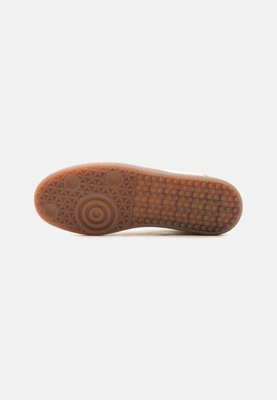 Semelle de chaussure avec une surface en caoutchouc texturée présentant des motifs circulaires et ondulés sur un fond clair.