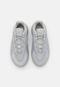 Vaaleanharmaat urheilukengät, joissa on tekstuuripinnoitteita, pyöreä muoto, nauhat ja hillitty logo kengän kielellä, varustettuna pehmustetulla pohjalla.