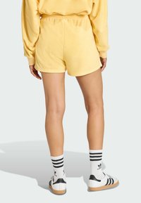 Žlté krátke teri šortky s voľným strihom a elastickým pásom, skombinované s čierno-bielymi prúžkovanými ponožkami a klasickými bielymi teniskami.