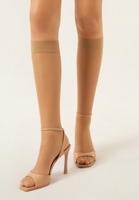 Nackte Oberschenkelstrümpfe mit glatter Textur, elastischem Bund oben, kombiniert mit hellen, nudefarbenen Open-Toe-Pumps mit hohen Absätzen.