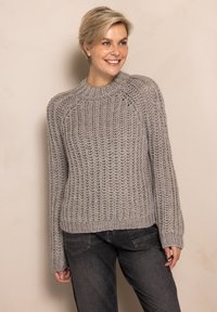 Light gray knitted sweater with a textured pattern, wide sleeves, and a crew neckline. Paired with dark gray pants.