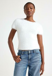 Hvid kortærmet sweater lavet af blødt materiale, med en afslappet pasform og rund halsudskæring, parret med lyseblå høj talje jeans.