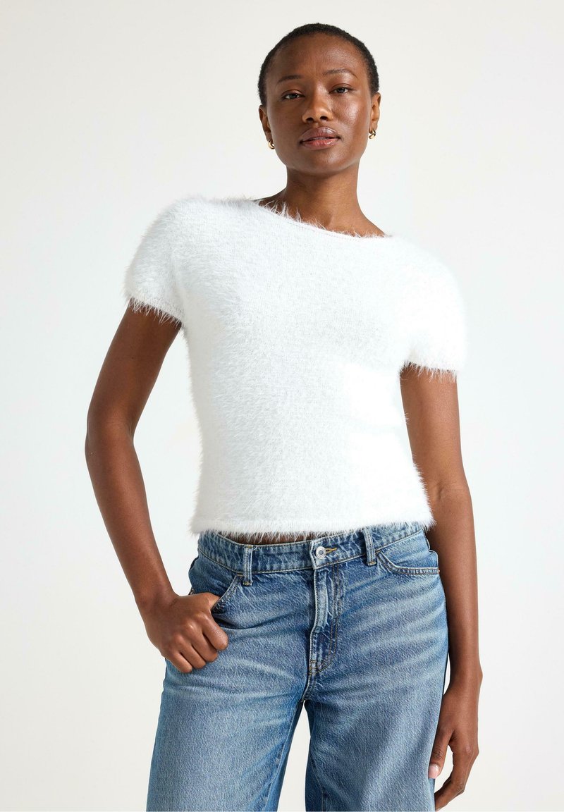 Hvid kortærmet sweater lavet af blødt materiale, med en afslappet pasform og rund halsudskæring, parret med lyseblå høj talje jeans.