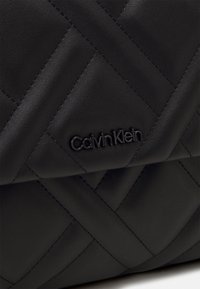 Borsa a tracolla in pelle trapuntata nera caratterizzata da una texture liscia e un discreto logo "CalvinKlein" in metallo scuro sulla parte frontale.