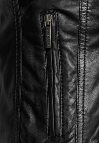 Détail d'une veste en cuir noir avec une poche zippée, des coutures visibles et une finition texturée, mettant en valeur le matériau doux et souple.