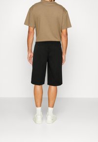 Černé kraťasy se rovnými nohavicemi, dvěma zadními kapsami a jemnými červenými detaily, v kombinaci s béžovým tričkem a bílými teniskami.