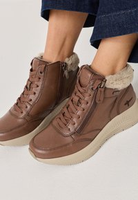 Hnědé kožené vysoké boty s zipovým uzávěrem a měkkou kožešinovou podšívkou, se strukturovanou podrážkou a zesílenými švy.