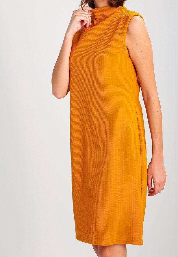 Robe sans manches en maille côtelée orange avec un col montant portée par une personne atteignant juste au-dessus des genoux.