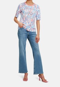 Kortärmad, rundhalsad tröja med ett blommönster i blått och rosa, kombinerad med ljusblå urtvättade jeans och rosa klacksandaler.