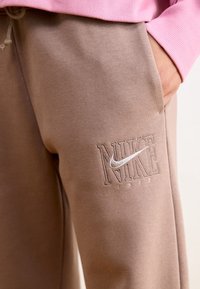 Bruna sweatpants med broderad Nike-logotyp och detalj "1972", har en mjuk textur och sidofickor.