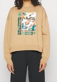 Felpa color kaki con design cropped, caratterizzata da una grafica astratta colorata e testo in grassetto. Realizzata in tessuto morbido con vestibilità comoda.