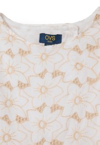 Top de tejido blanco con bordado floral beige, cuello redondeado y etiqueta que dice "OVS kids." Diseño texturizado con patrones de flores intrincados.