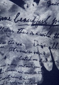 Marinblå tyg med en strukturerad, abstrakt design som har handskriven text i kontrasterande mörk bläck. Mönstret inkluderar suddiga element och virvlar.