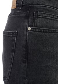 Jean en denim noir avec une texture lisse, des coutures visibles, des poches standard et un petit logo métallique.