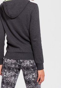 Sudadera gris con capucha, que presenta puños y dobladillo acanalados, combinada con leggings de patrón en blanco y negro, que muestran un diseño texturizado.
