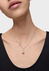 Collar de cadena de plata que presenta dos colgantes: un cristal transparente y una gema naranja redonda, reposando sobre un escote negro.