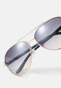 Aviator-Sonnenbrille mit verlaufenden grauen Gläsern, goldfarbenem Metallrahmen und schwarzen Bügelspitzen. Verfügt über ein Nasenpolster für Komfort und klare Akzente.