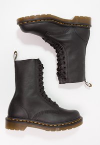 Bottes noires en cuir à lacets avec surpiqûres jaunes et semelles en caoutchouc brun translucide, vues de côté et de dessus sur un fond blanc.