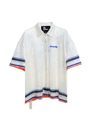 Hombre con rastas que lleva pantalones cortos blancos y camisa grande a juego con rayas azules y naranjas, diseño de ojo azul en la espalda y calcetines blancos.