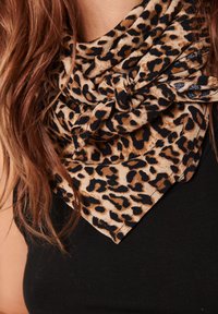 Leopardprint tørklæde lavet af blødt stof, med tan og sorte pletter, knyttet foran, i en trekantet form.