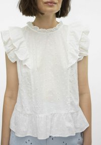 Balta blusa su volanų rankovėmis, aukštu kaklu ir tekstūruota medžiaga su mažomis siuvinėjimo detalėmis bei peplum apatine dalimi.