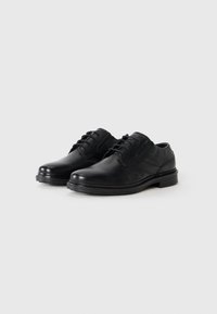 Zapatos de vestir de cuero negro con textura suave, punta redonda, diseño con cordones y un tacón bajo apilado. Sutiles acentos de costura en los laterales.
