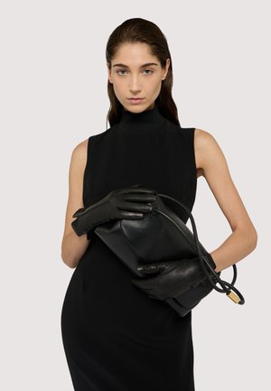 Black leather clutch bag held with black leather gloves. The model wears a sleeveless black dress, set against a neutral background.