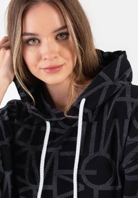 Czarna bluza z kapturem z geometrycznym wzorem w odcieniach szarości, dużą przednią kieszenią, sznurkami oraz kontrastującym białym przeszyciem.