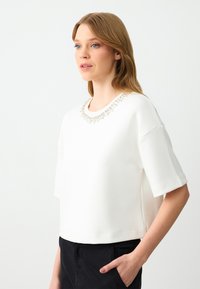 Witte top met korte mouwen, voorzien van een ronde halslijn versierd met decoratieve rhinestones, een gladde textuur en een ontspannen pasvorm.