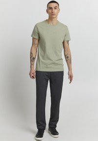 Camiseta de algodón verde claro con cuello redondo y texto en relieve. Combinada con pantalones oscuros de corte slim y zapatillas negras.