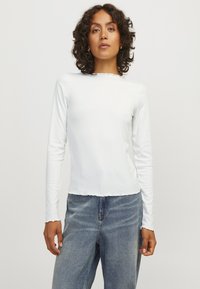 White long-sleeve shirt with ribbed texture and a scalloped hem, paired with high-waisted blue denim jeans. Simple and fitted design.