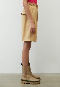 Pantaloni corti in cotone beige con vita elasticizzata e tasche laterali, abbinati a stivaletti beige a caviglia con suola spessa e robusta e linguette di estrazione.
