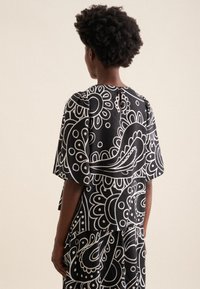 Blusa a fantasia bianco e nero con maniche corte, caratterizzata da un collo rotondo e un dettaglio a taglio sul retro. Tessuto testurizzato.
