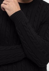 Pull noir en maille torsadée avec col et poignets côtelés, présentant des motifs texturés sur tout le tissu pour plus de chaleur.