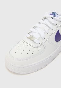 Vita lädersneaker med lila Nike swoosh, rund tå, perforerat övre material för andningsförmåga, metallflik för snörningen och texturerad gummisula.