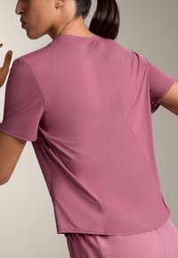 Krátký rukáv sportovní top v barvě mauve, s texturovanou zadní částí a malými ventilačními otvory. Hladká tkanina, volný střih, minimální švy.