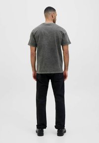 Sivi mineral-nošeni t-shirt s kratkim rukavima, u kombinaciji s crnim hlačama. Vidljivo šivanje i opušteni kroj. Obuća je od crne kože.