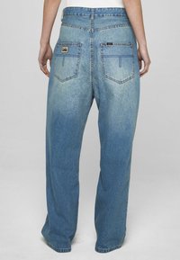 Svetlo modre kavbojke iz jeansa z ohlapnim krojem, z dvema zadnjima žepoma, etiketo na pasu in rahlim bledenjem proti dnu.