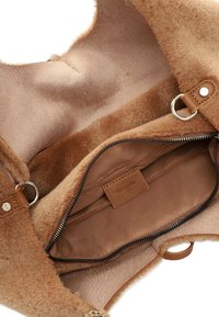 Intérieur de sac à main marron avec une texture douce en fourrure, doublure beige, poche zippée et accents en cuir. Comprend une étiquette de marque et des quincailleries en métal.