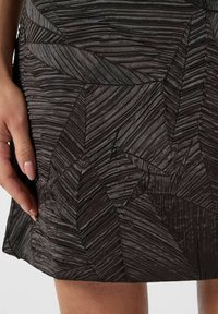 Texturerad svart tygkjol med ett veckmönster som liknar överlappande löv. Materialet verkar lätt och något glansigt.