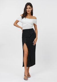 Witte off-shoulder top gecombineerd met een zwarte kanten maxi rok met een hoge split, gedragen met zwarte sandaletten met bandjes.